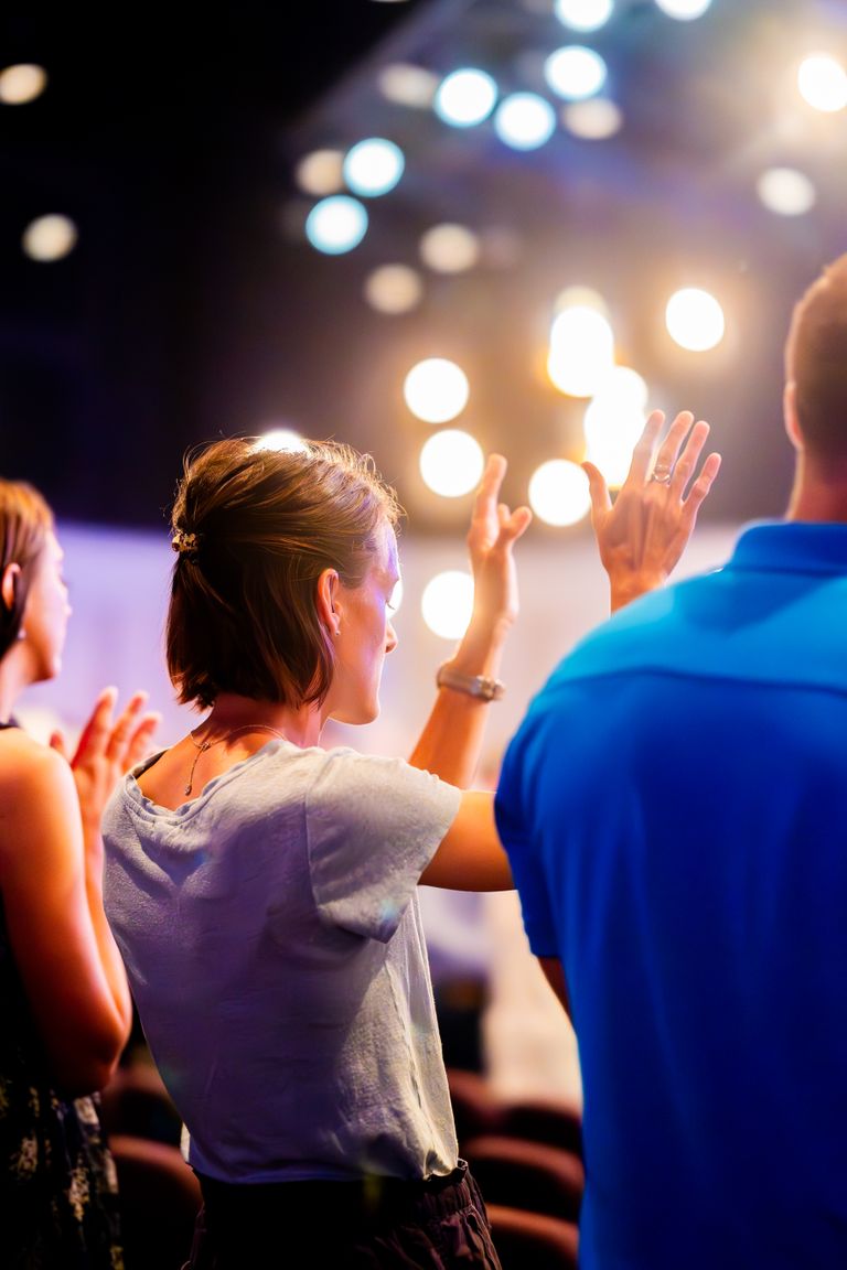 People raising hands in worship at a lively concert with vibrant lights.