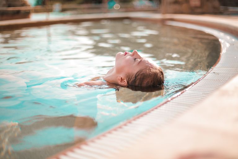 A woman enjoys peaceful relaxation while floating in a sunny outdoor pool, captured in soft natural light.