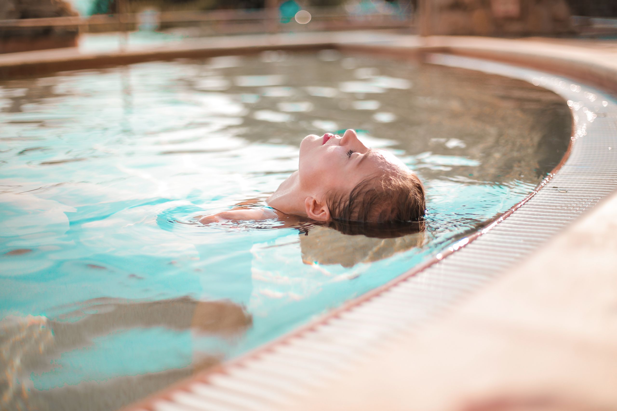 A woman enjoys peaceful relaxation while floating in a sunny outdoor pool, captured in soft natural light.