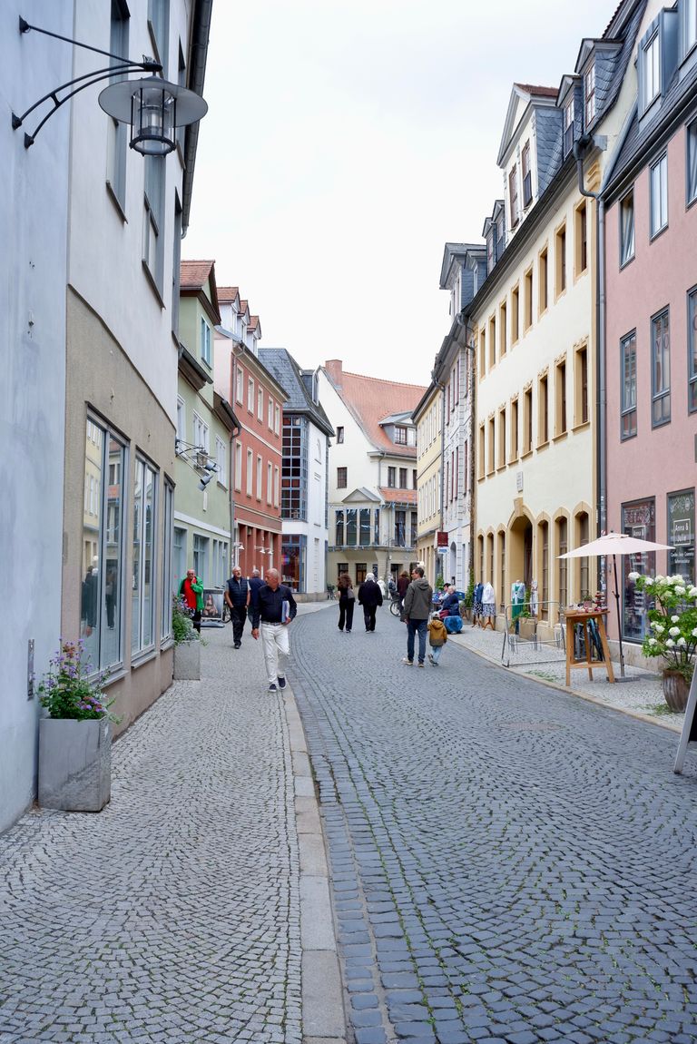 View of a picturesque cobblestone street in Weimar, Germany, showcasing colorful architecture and people strolling.