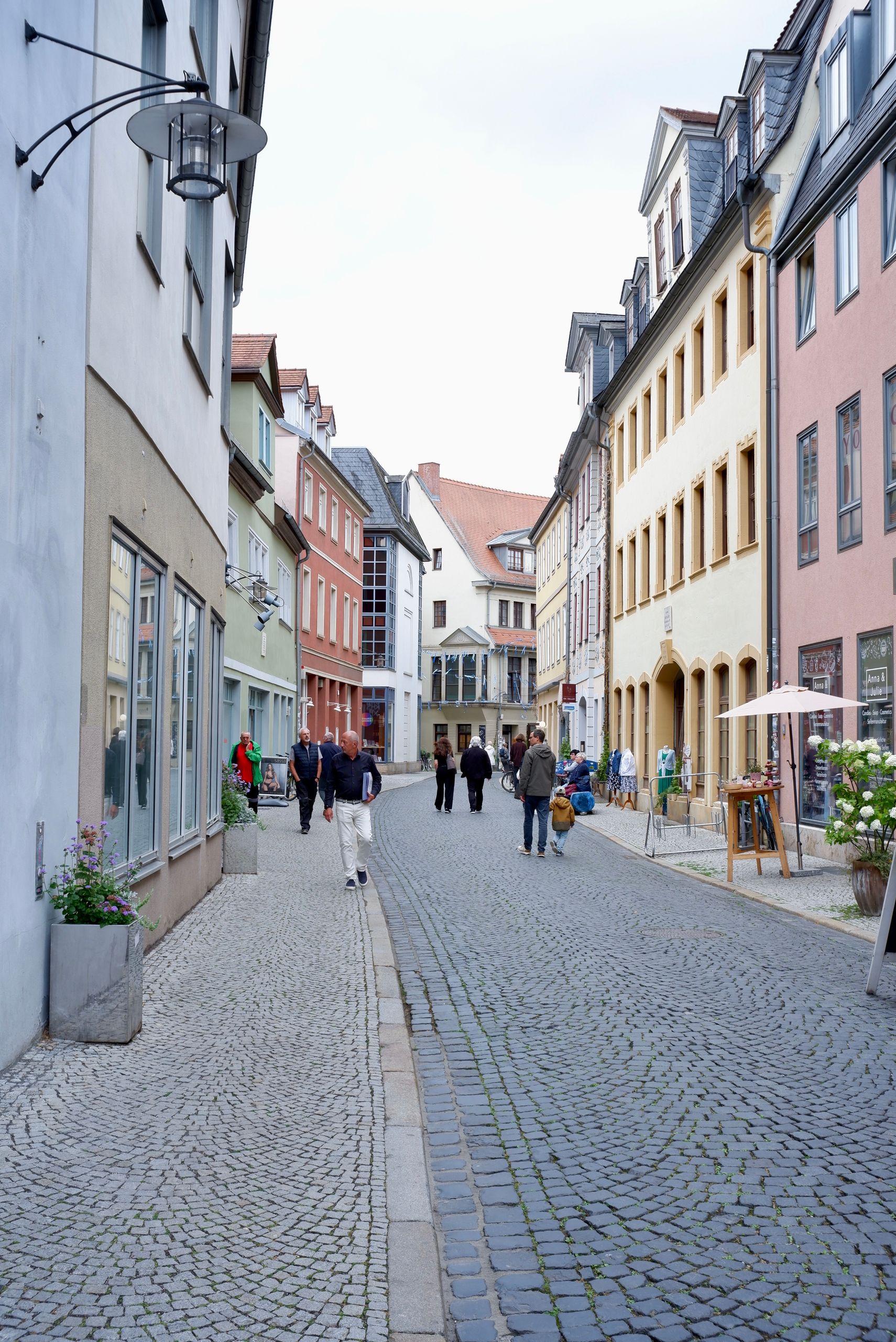 View of a picturesque cobblestone street in Weimar, Germany, showcasing colorful architecture and people strolling.